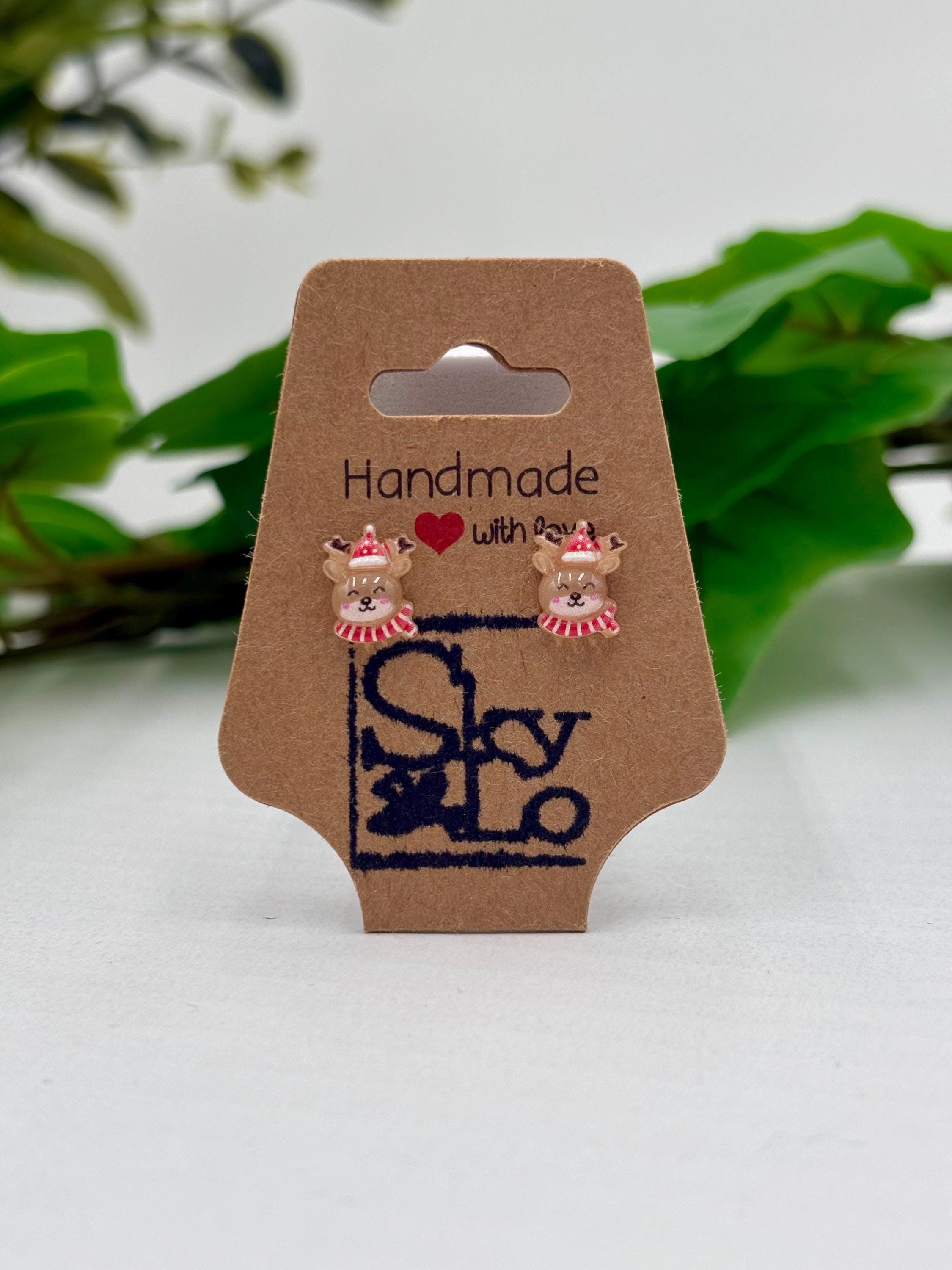 Pair of Reindeer earrings on a 'Handmade with Love' branded card with a plant in the background.