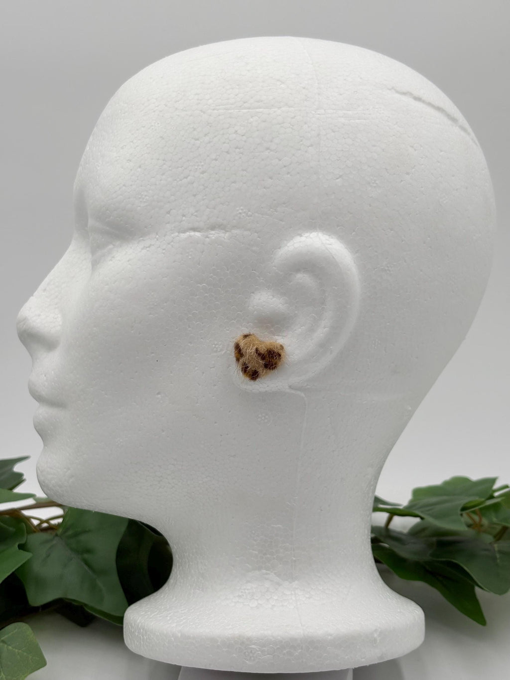 Mannequin head with a light brown faux fur leopard print earring on a gray background