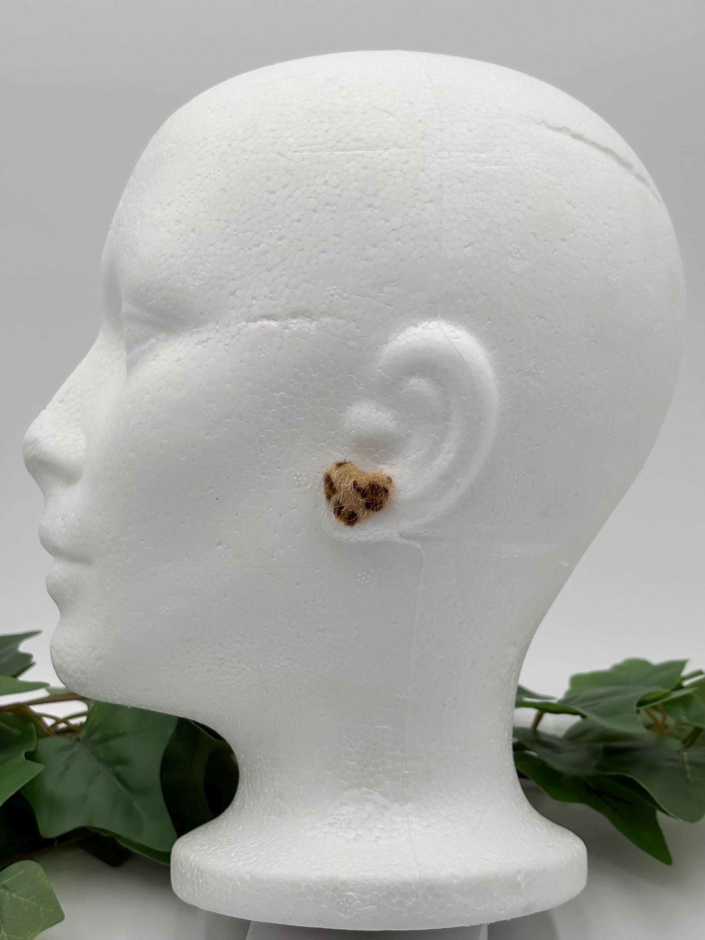 Mannequin head with a light brown faux fur leopard print earring on a gray background