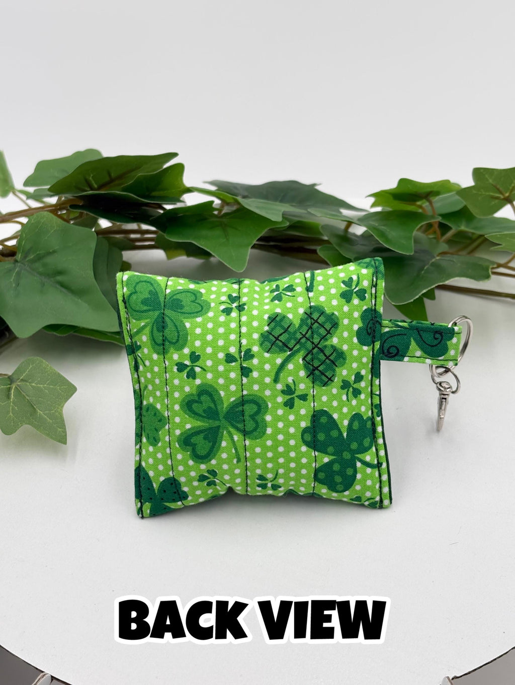 Back of a Small quilted headphone holder pouch keychain with green shamrocks design on a white surface with green leaves with text "back view"