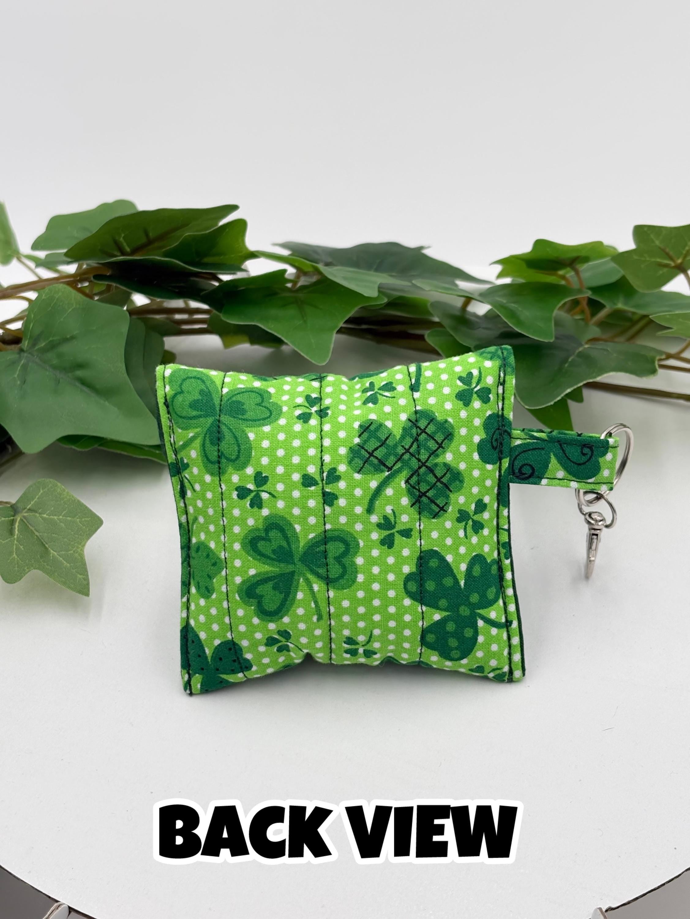 Back of a Small quilted headphone holder pouch keychain with green shamrocks design on a white surface with green leaves with text "back view"