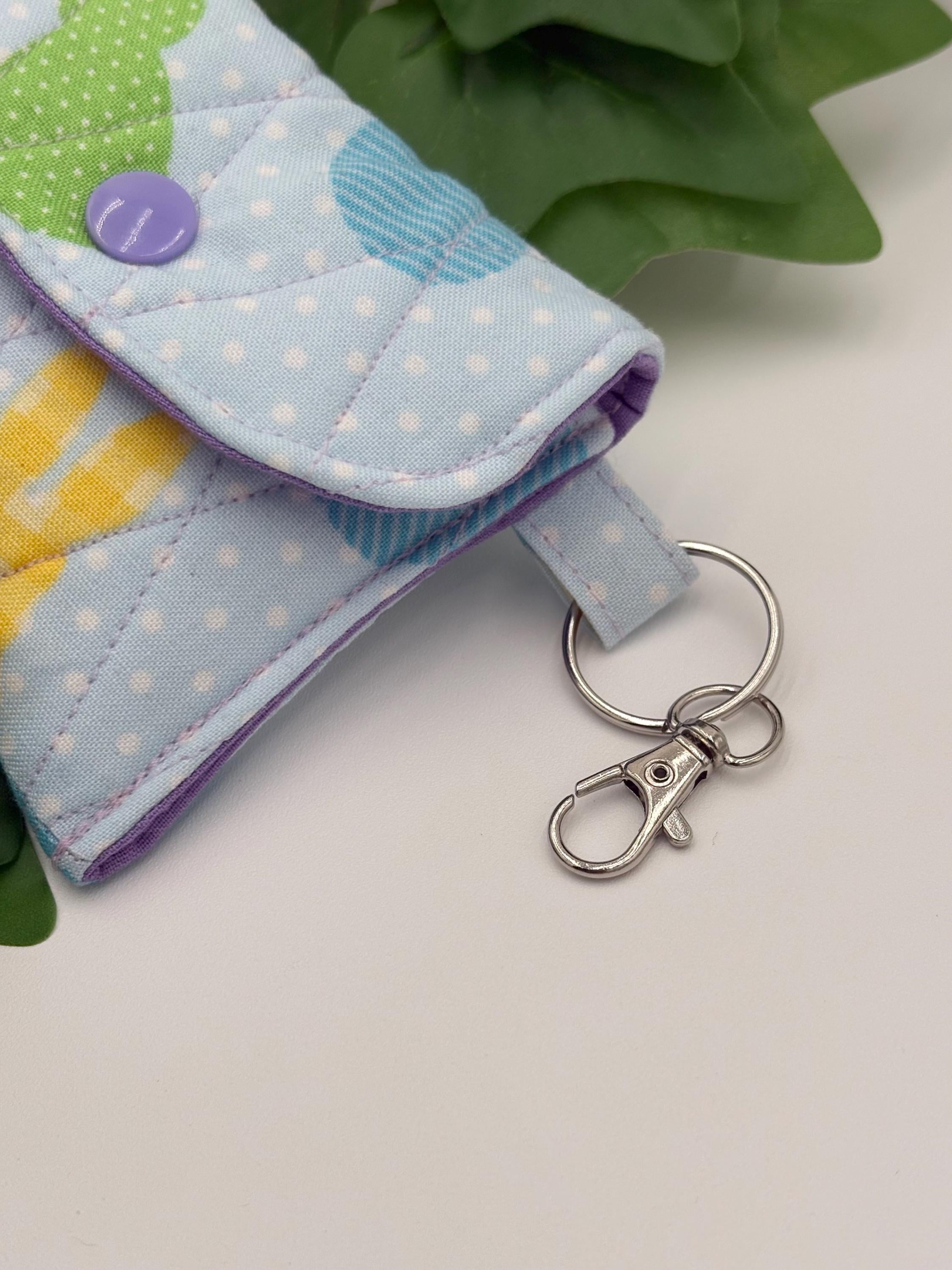 Close up of the lobster clasp keychain for a Small quilted headphone holder pouch keychain with colorful easter design on a white surface with green leaves.