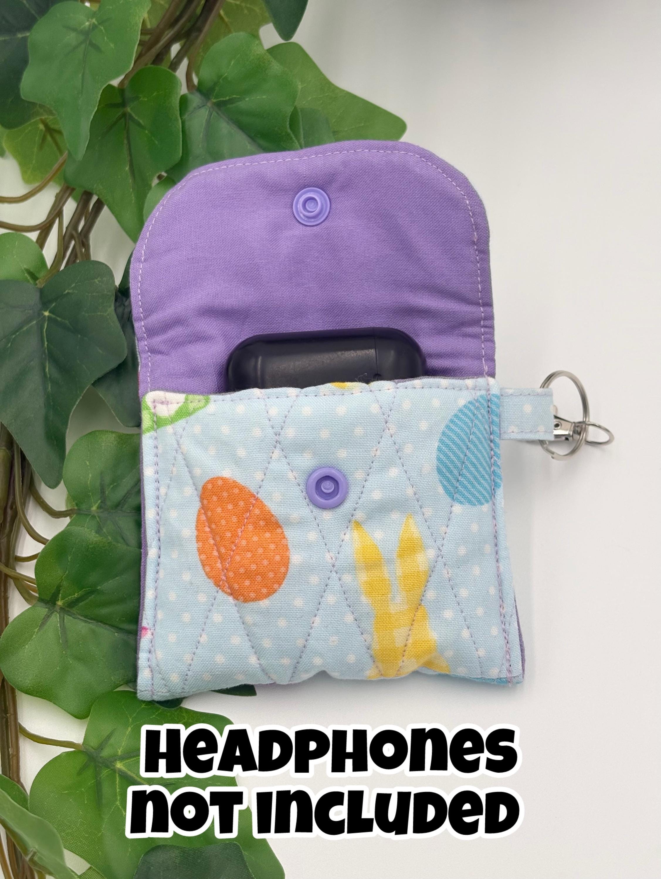 Opened Small quilted headphone holder pouch keychain with colorful easter design showing purpler liner with headphone case inside on a white surface with green leaves with text "Headphones not included"