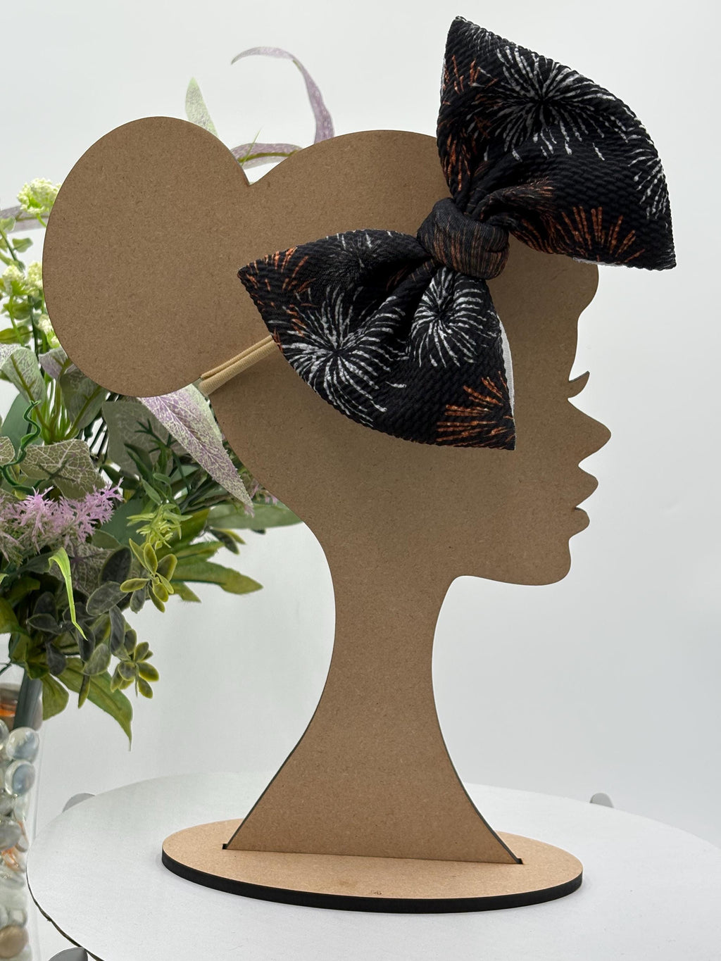 Black Nylon Headband with a decorative white and orange fireworks themed big bow on a mannequin head silhouette against a white background