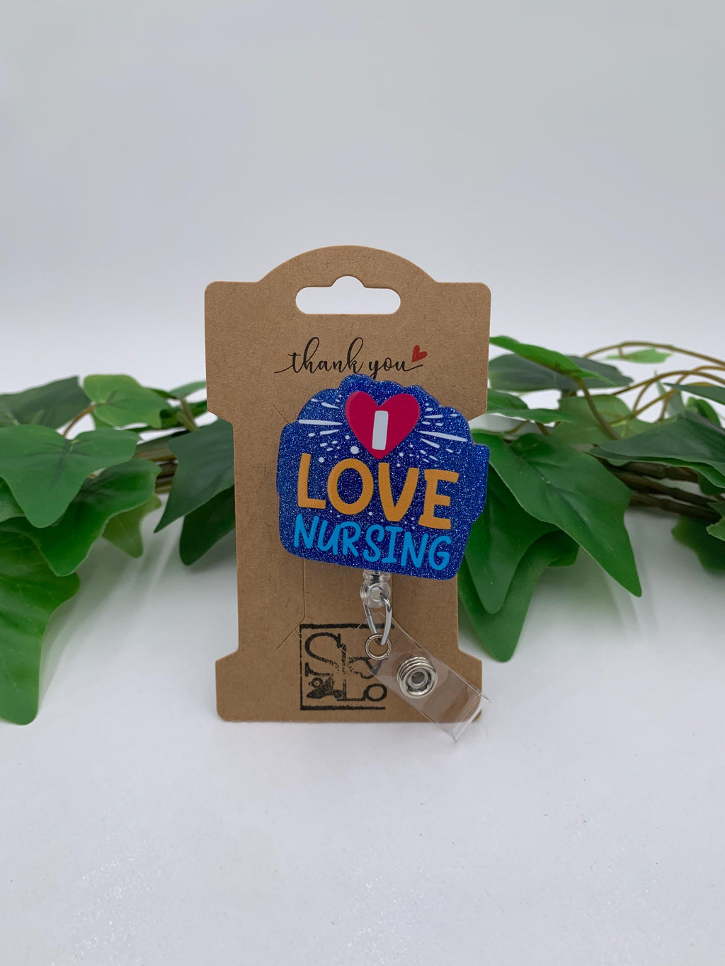 Badge Reel with 'I Love Nursing' text on a cardboard holder with green leaves in the background