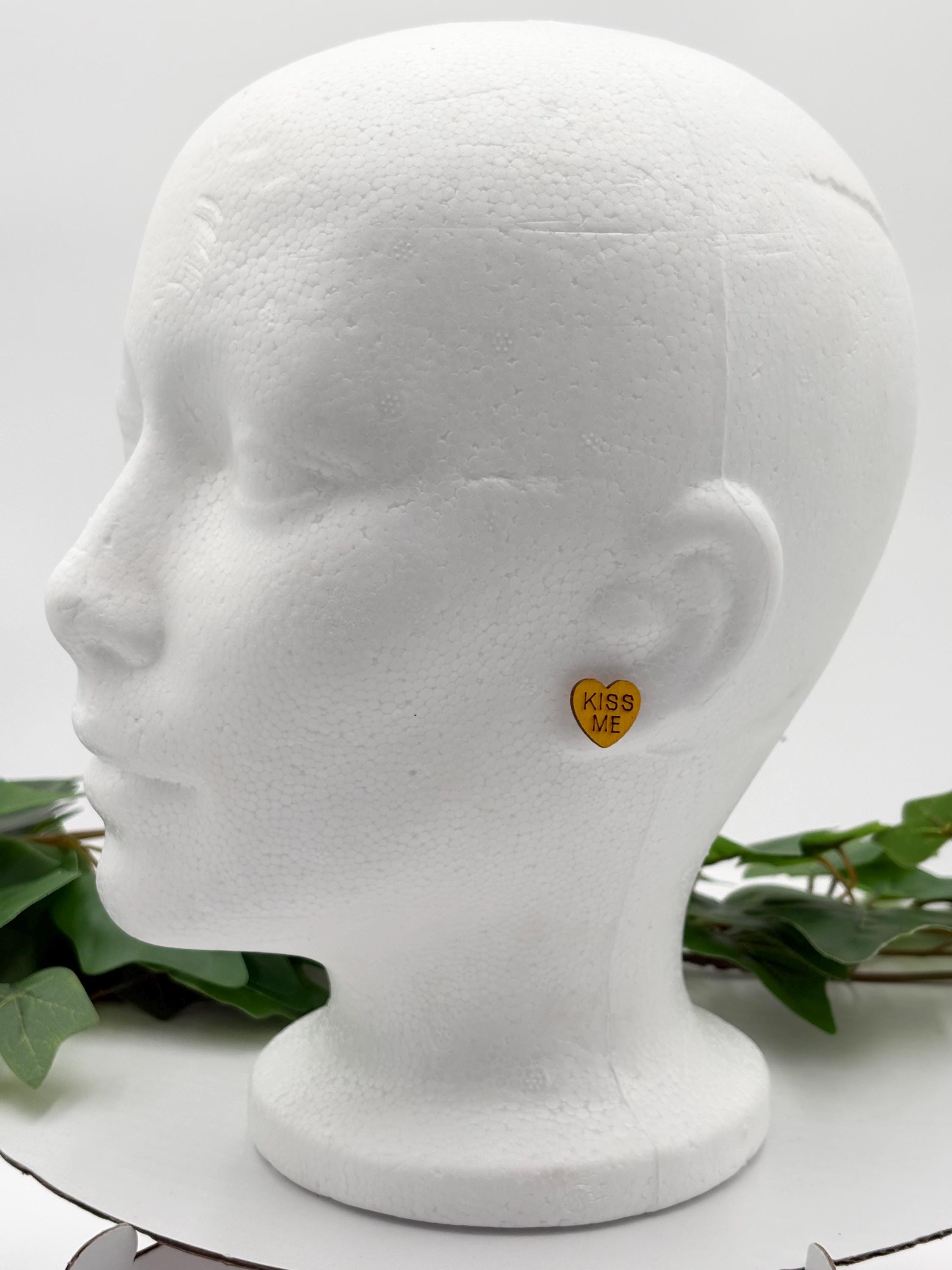 Mannequin head wearing a yellow heart-shaped earring with greenery in the background