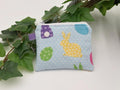 Small coin purse keychain with blue and pastel eggs and bunnies pattern on a white background with green leaves