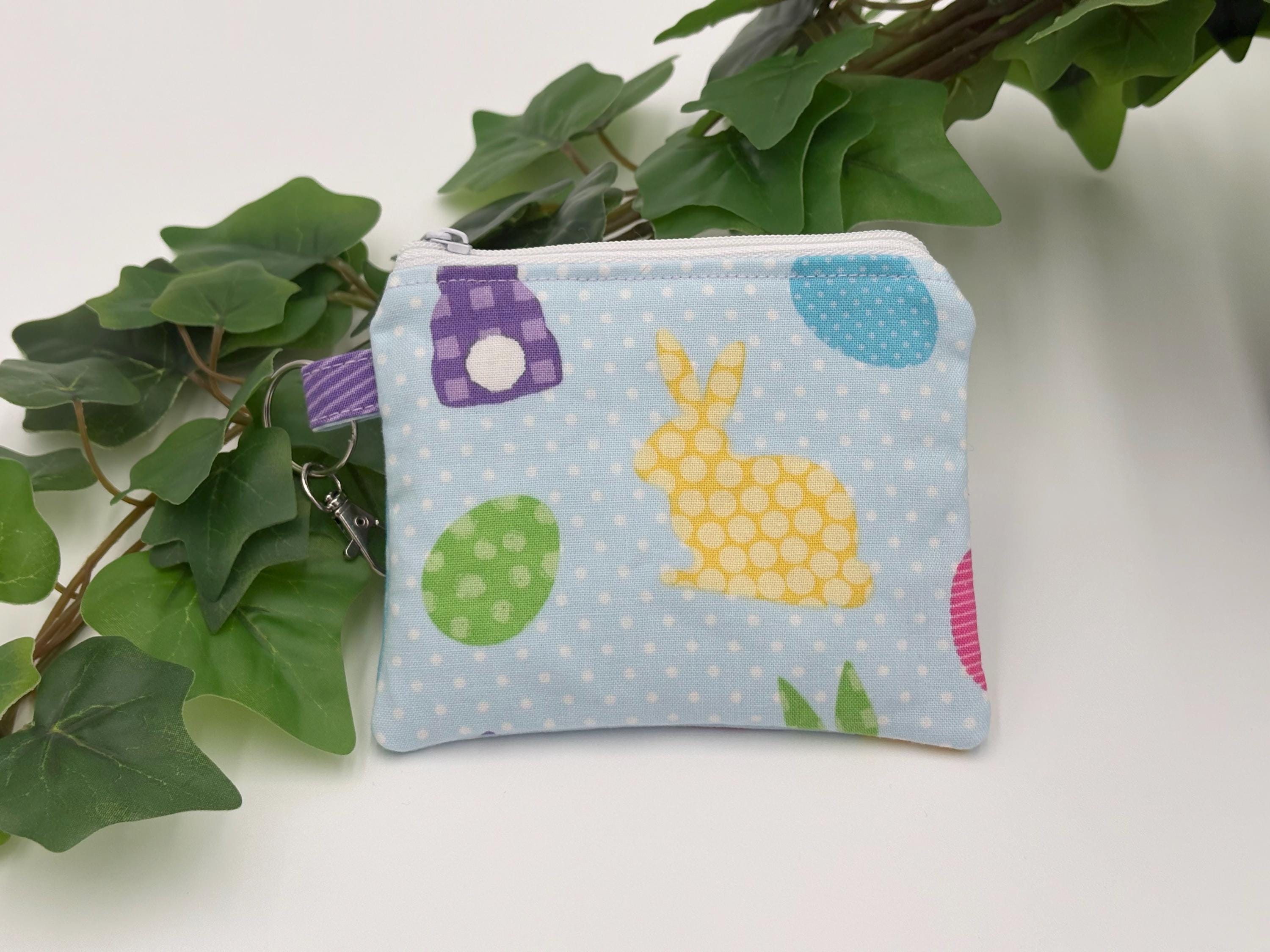 Small coin purse keychain with blue and pastel eggs and bunnies pattern on a white background with green leaves