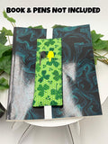 Green pen holder book mark with shamrock pattern on a marbled black and blue surface, with text 'Book & Pens Not Included'.