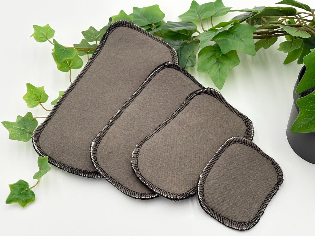 Set of gray reusable dog incontinence liners on a white surface with green leaves in the background