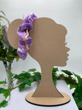 Cardboard head silhouette with a purple unicorn scrunchie on a white background with greenery.