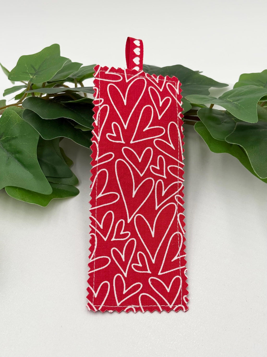 Red Fabric bookmark with white heart pattern on green leaves against a white background