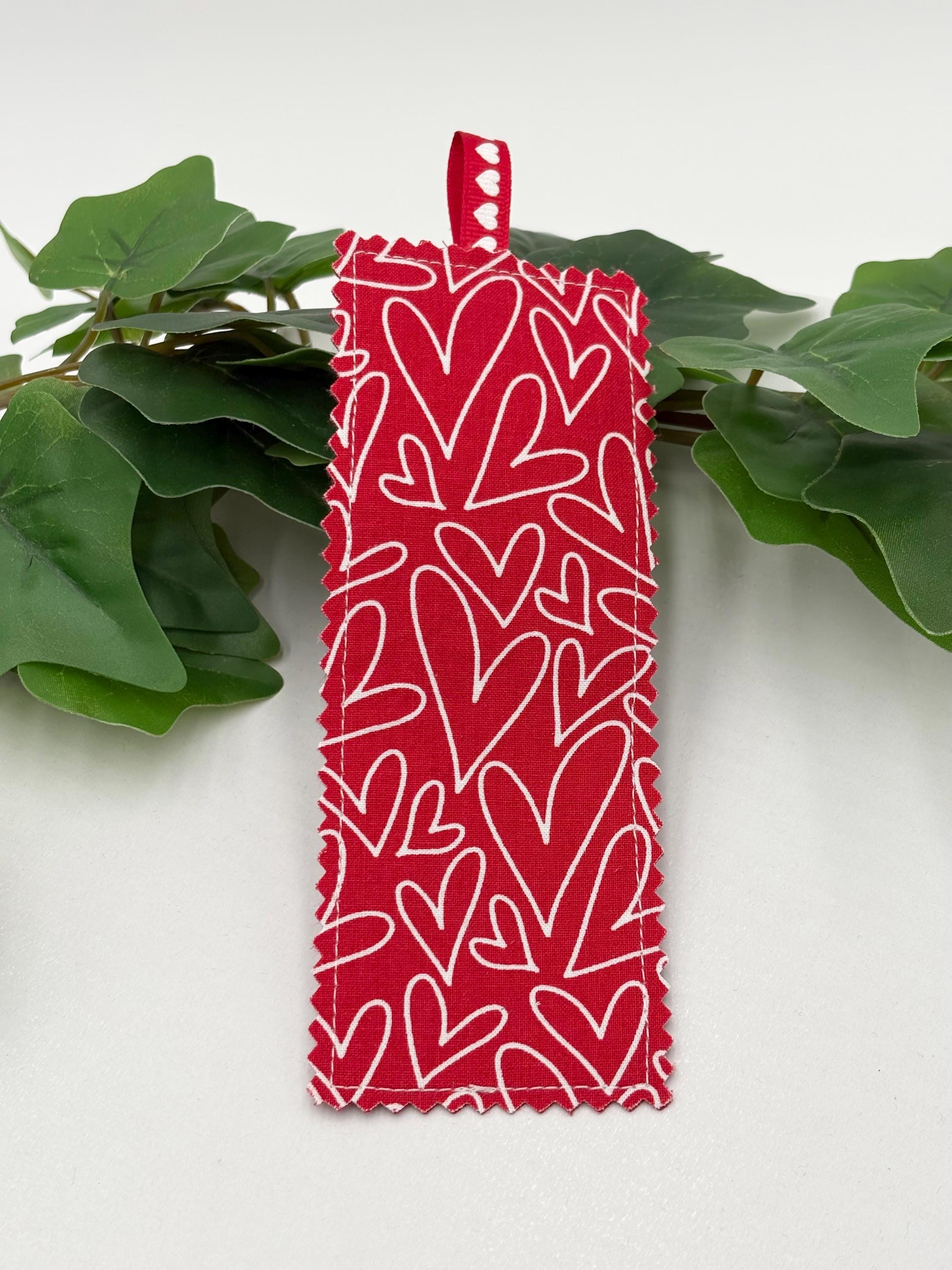 Red Fabric bookmark with white heart pattern on green leaves against a white background