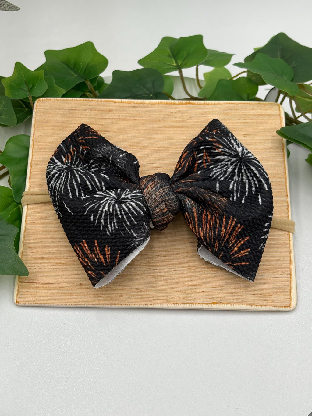 Black Nylon Headband with a decorative white and orange fireworks themed big bow on a wooden board against a white background