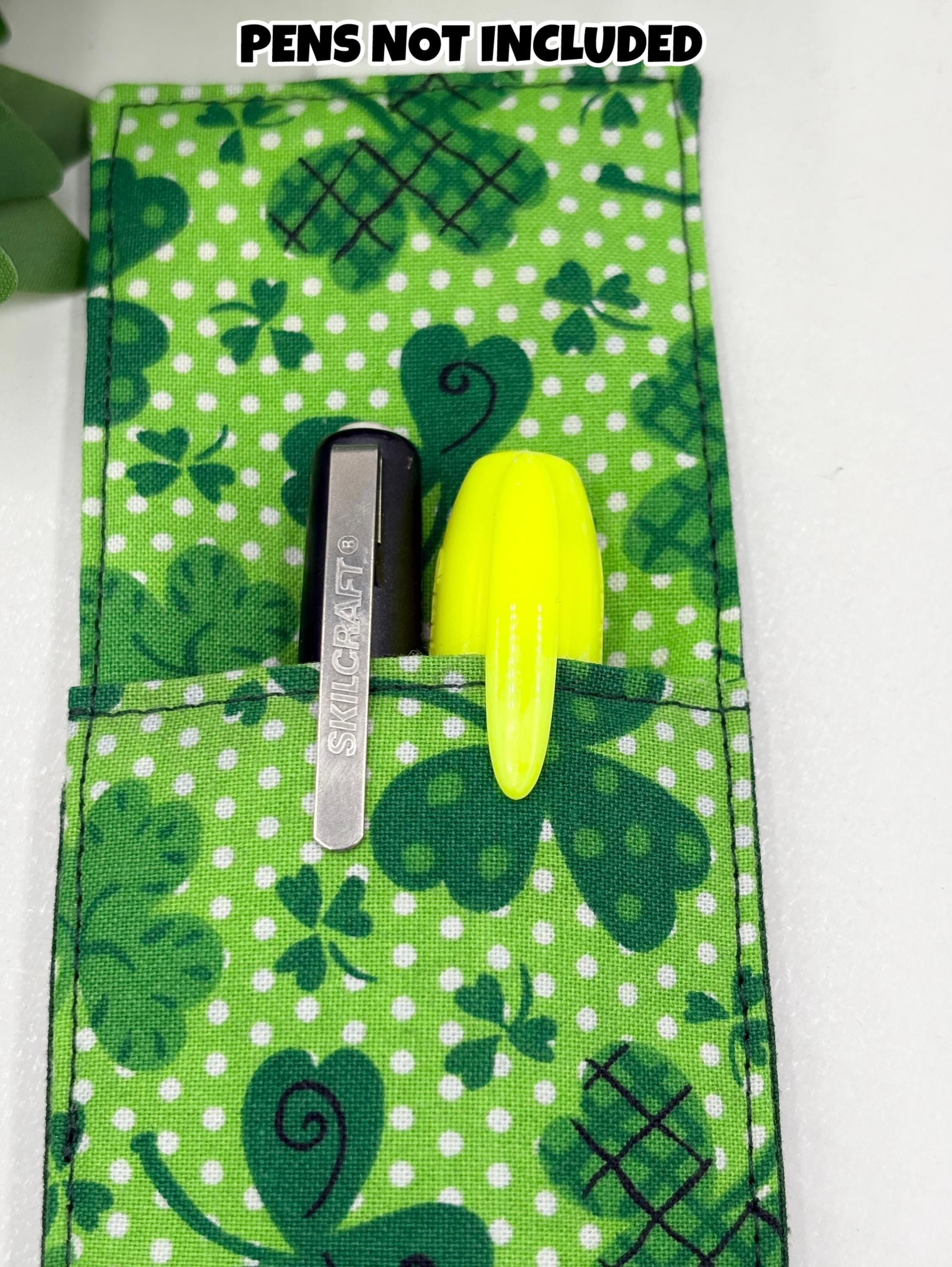 Green fabric pen holder bookmark with shamrock pattern containing stationery items on a white background.