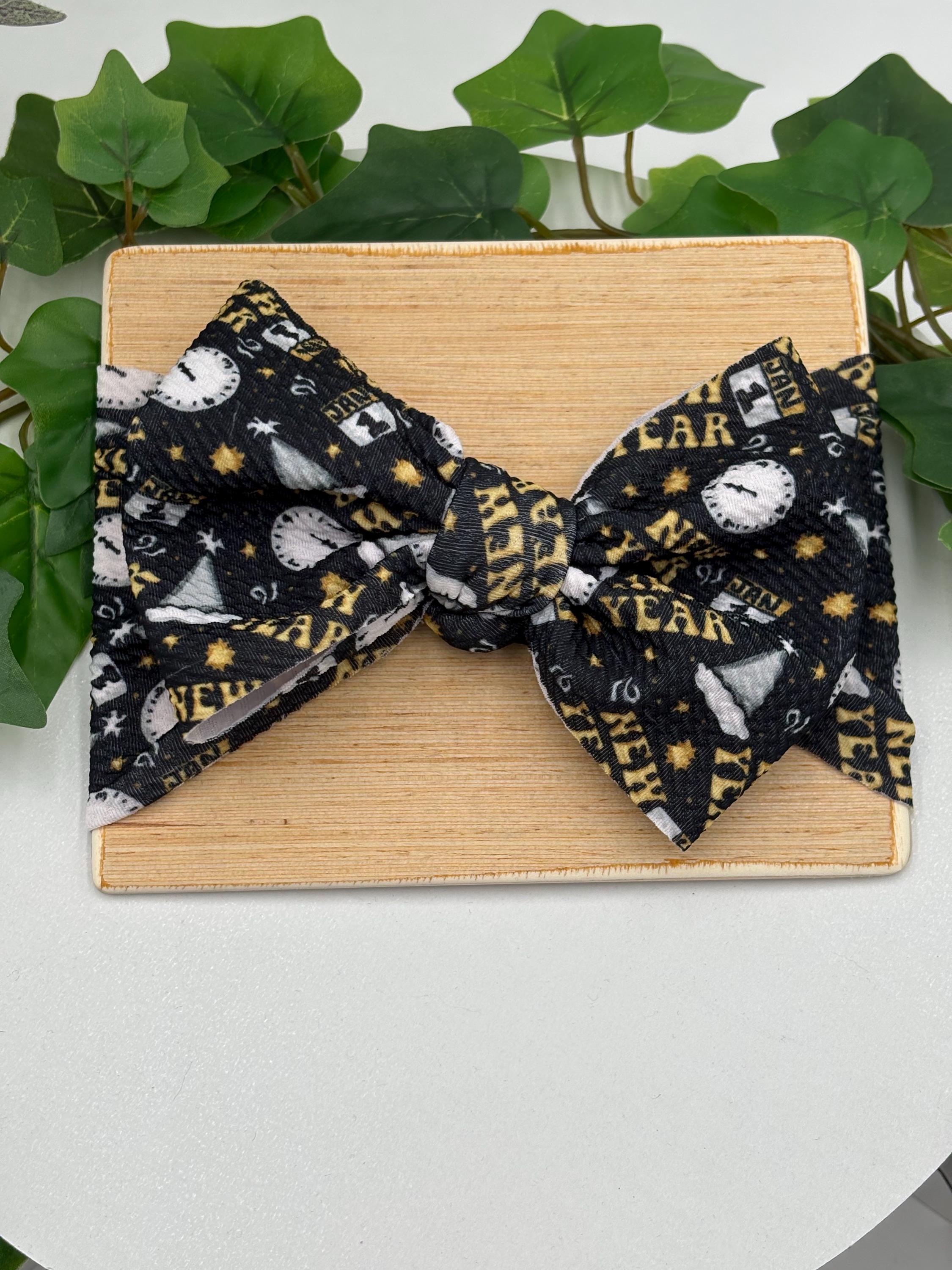 Black Headband with a decorative clocks and text "New Year" themed big bow on a wooden board against a white background
