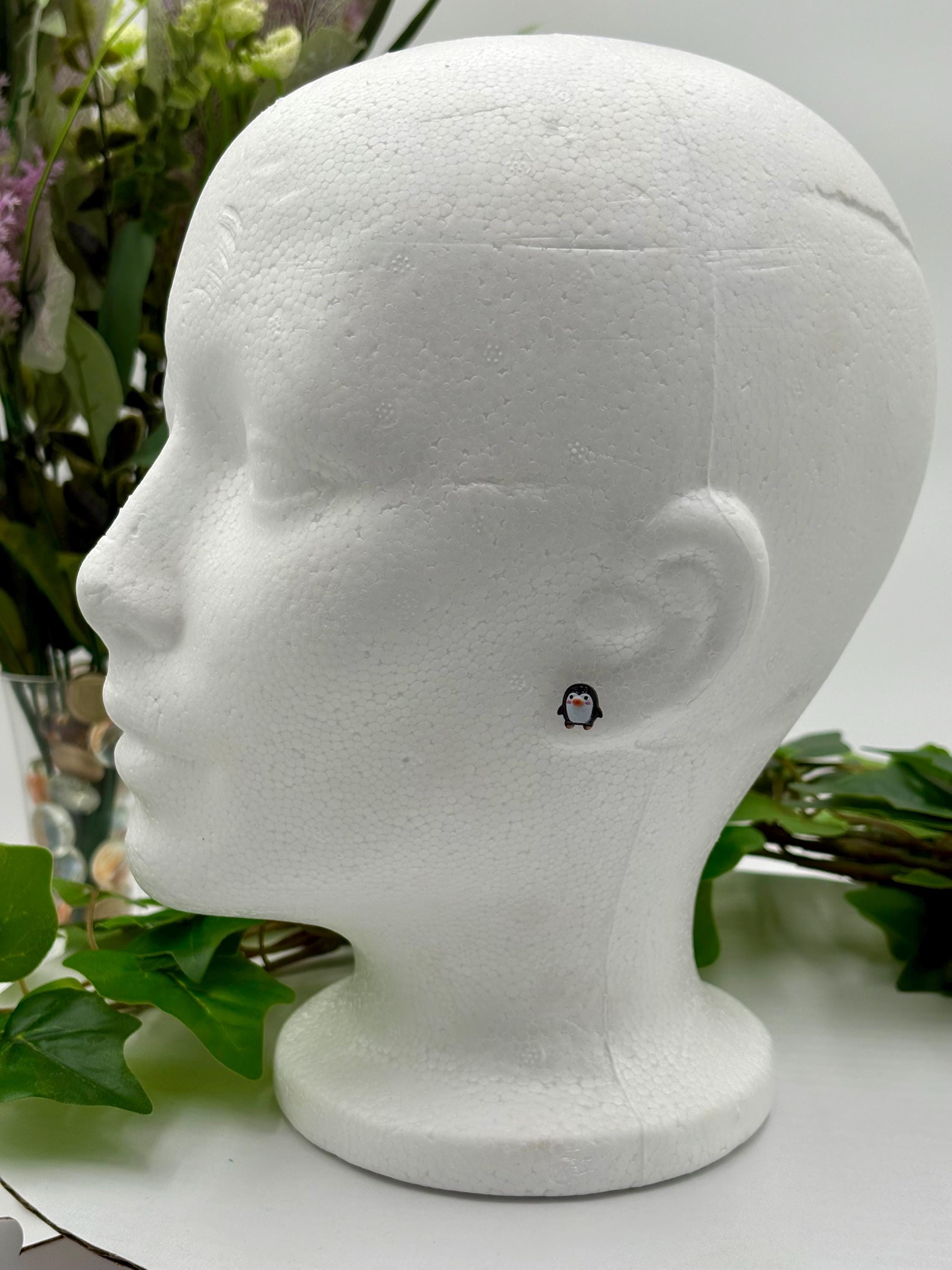 Penguin Earring displayed on a white mannequin head with greenery in the background
