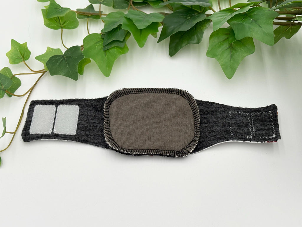 A gray reusable dog incontinence liner in a dog belly band on a white surface with green leaves in the background