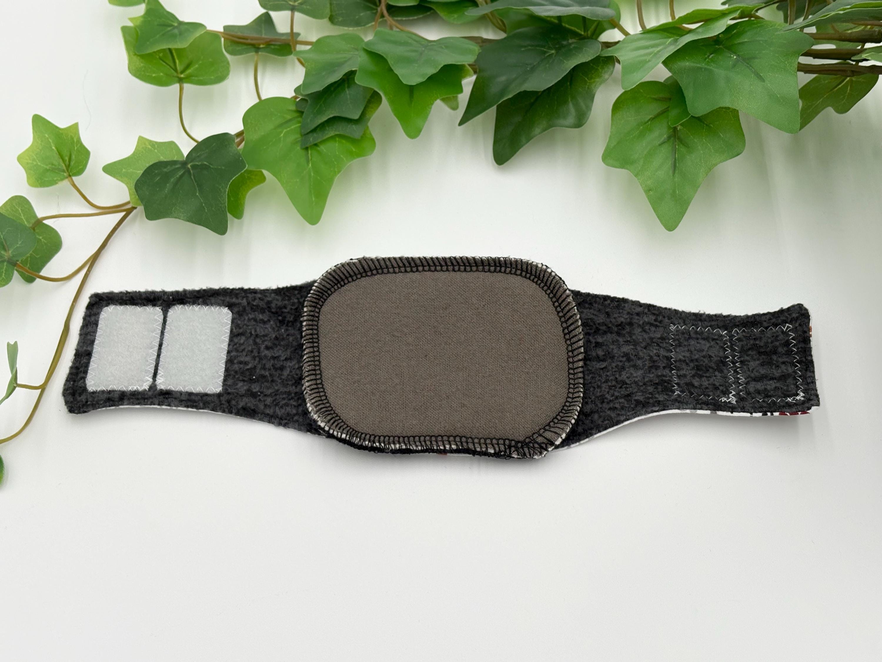 A gray reusable dog incontinence liner in a dog belly band on a white surface with green leaves in the background