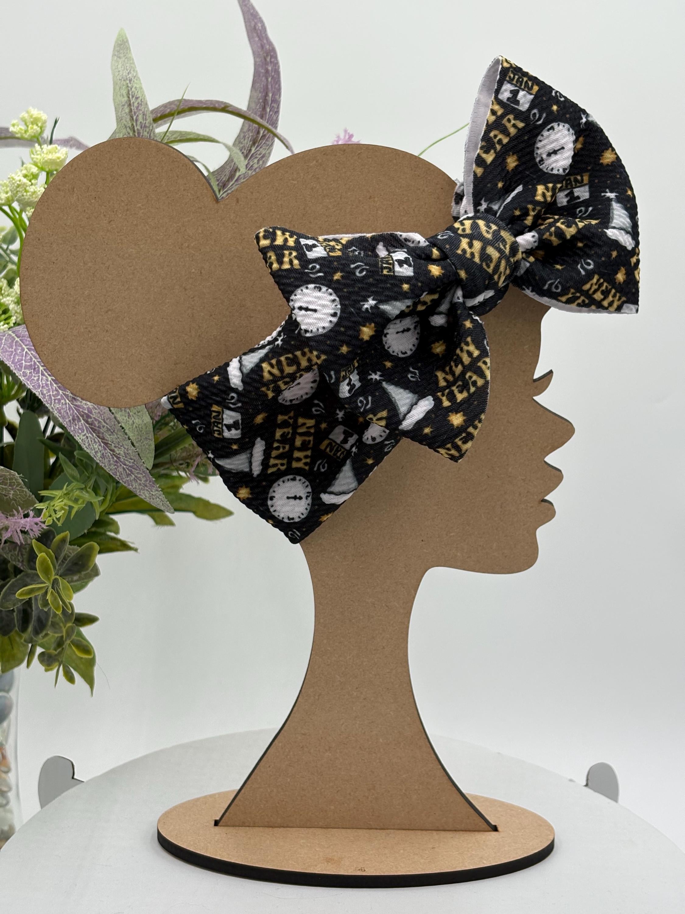 Black Headband with a decorative clocks and text "New Year" themed big bow on a mannequin head silhouette against a white background