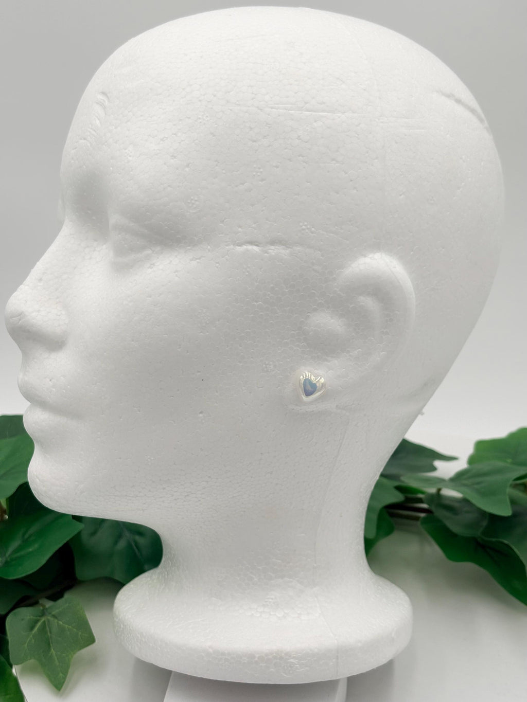 Mannequin head with white metallic heart shaped earrings on a white background