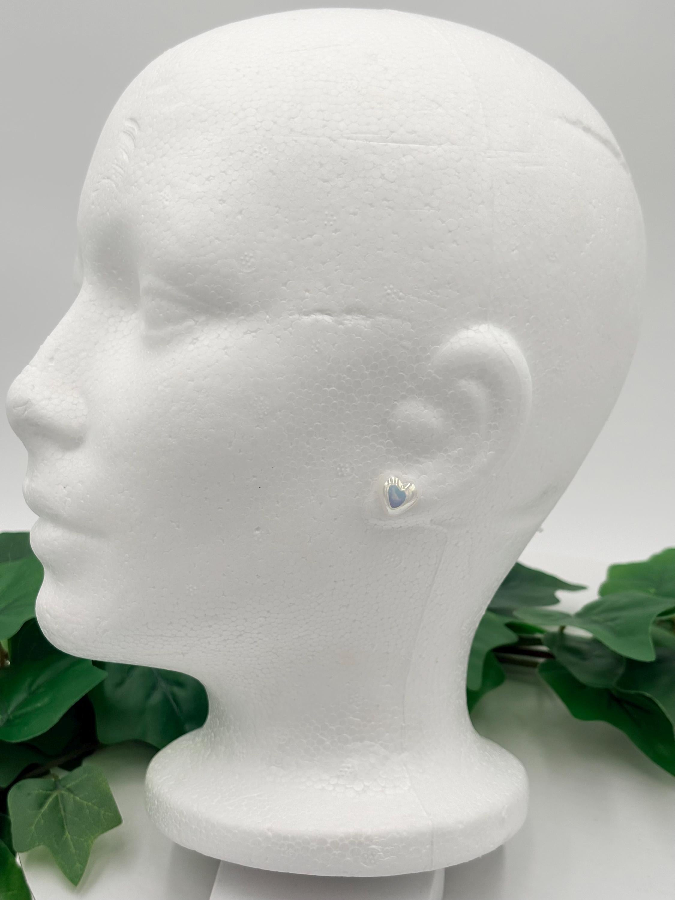 Mannequin head with white metallic heart shaped earrings on a white background