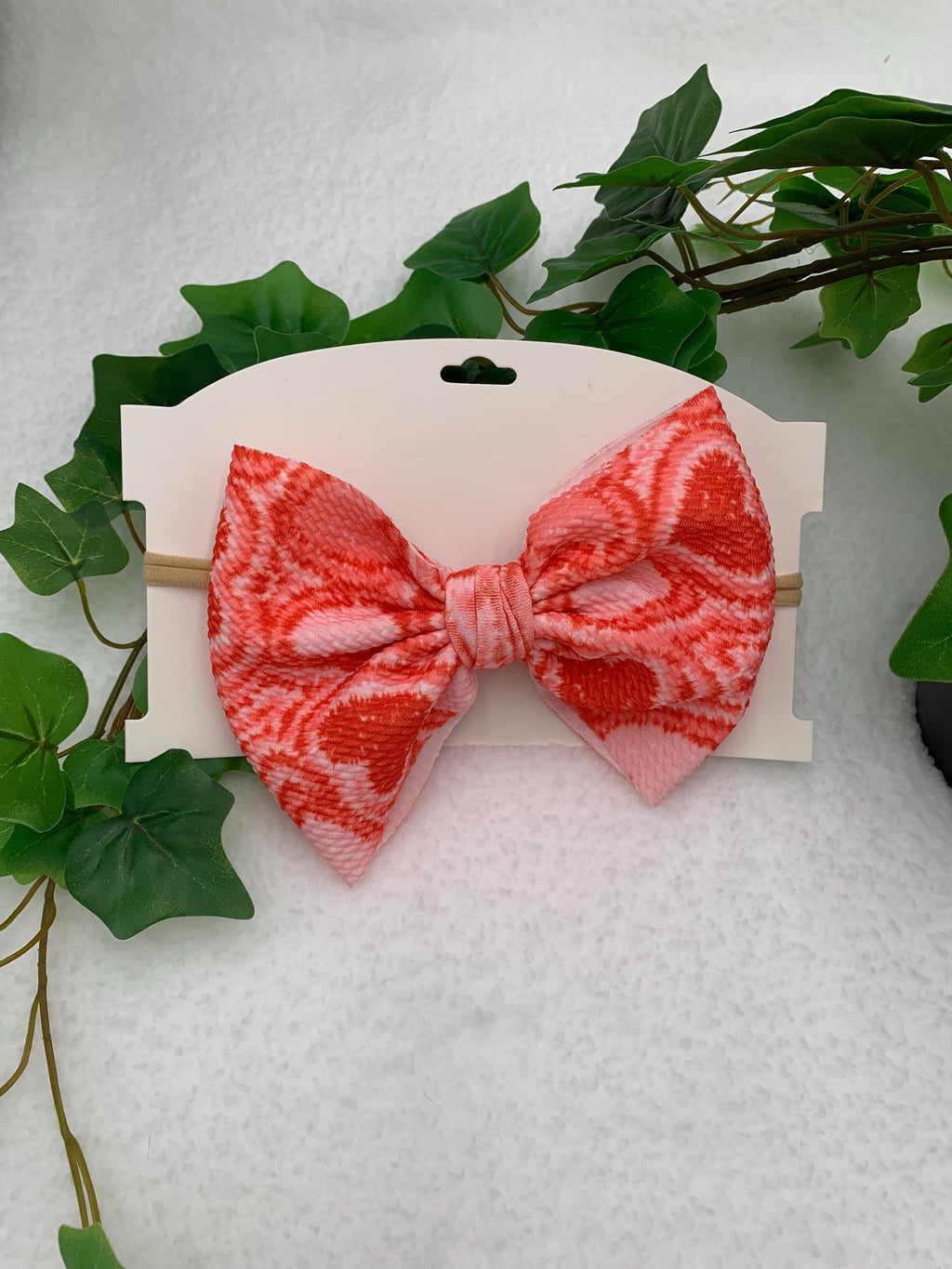 Pink Nylon Headband with a decorative hearts themed big bow on a white cardstock against a white background