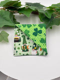 Green fabric square corner bookmark with gnome and shamrock pattern on a white surface with green leaves.