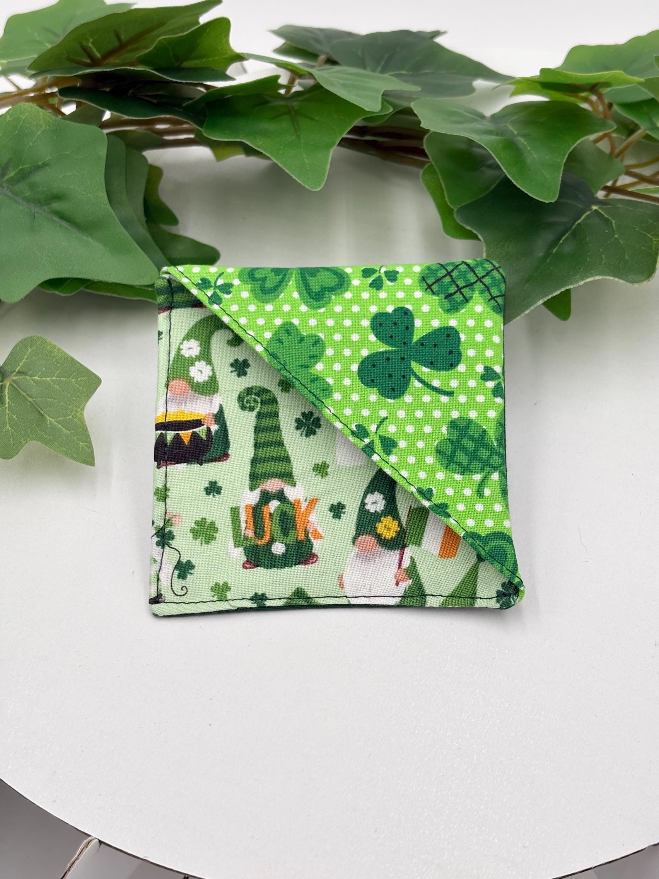 Green fabric square corner bookmark with gnome and shamrock pattern on a white surface with green leaves.