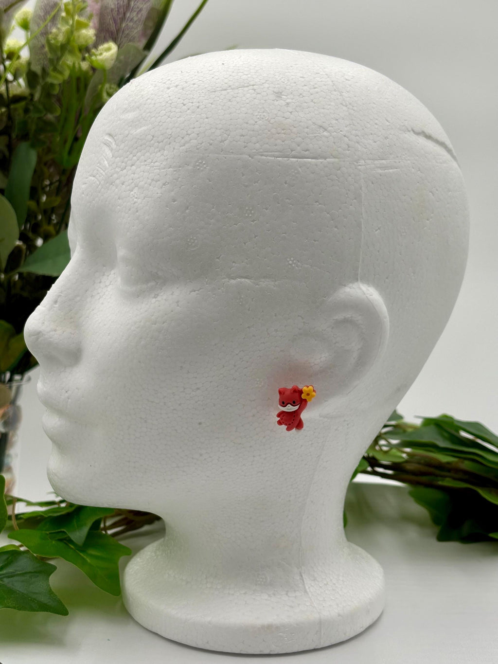 Mannequin head with a small red fox-shaped earring on a white background
