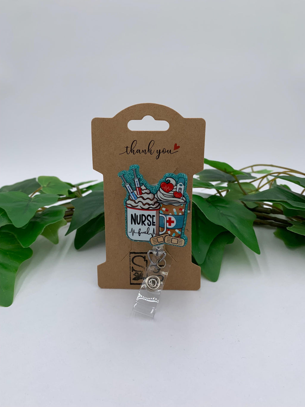 Nurse-themed badge holder with decorative elements on a cardboard backing, surrounded by green leaves.