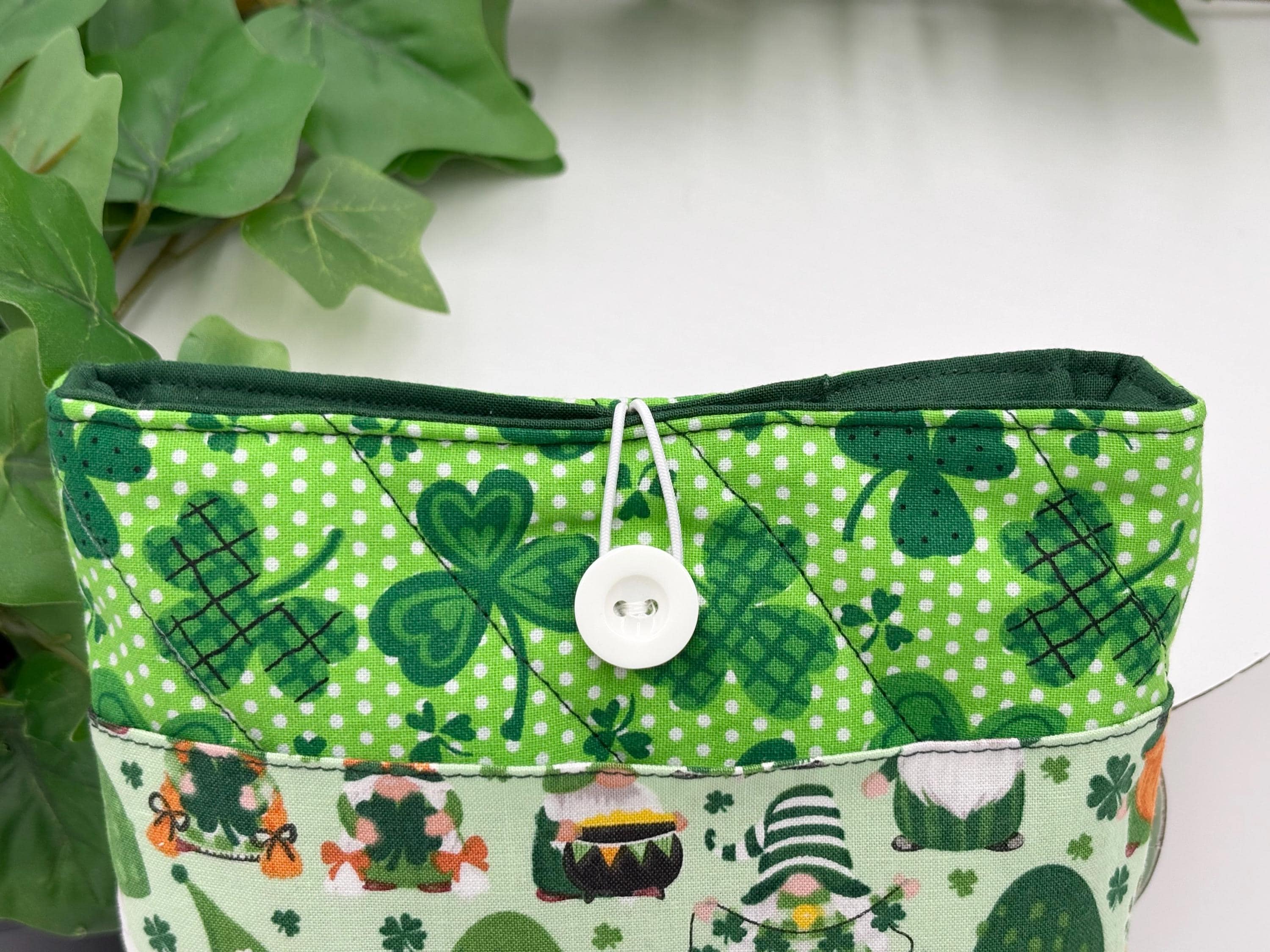 Green saint Patrick’s day gnomes and clovers patterned book sleeve showing button and elastic closure with white background and plants 