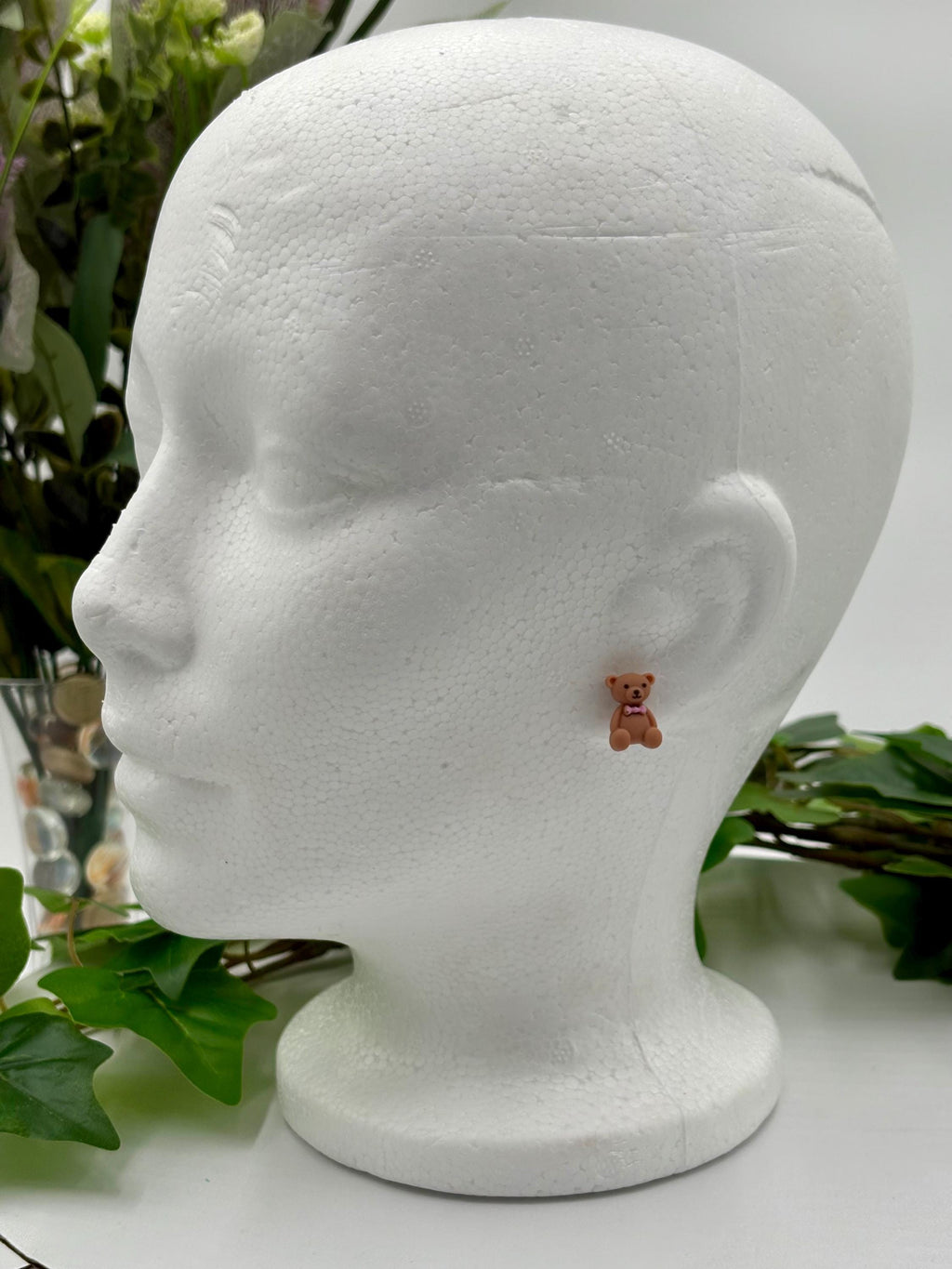 Teddy bear earrings on a mannequin head with green leaves in the background