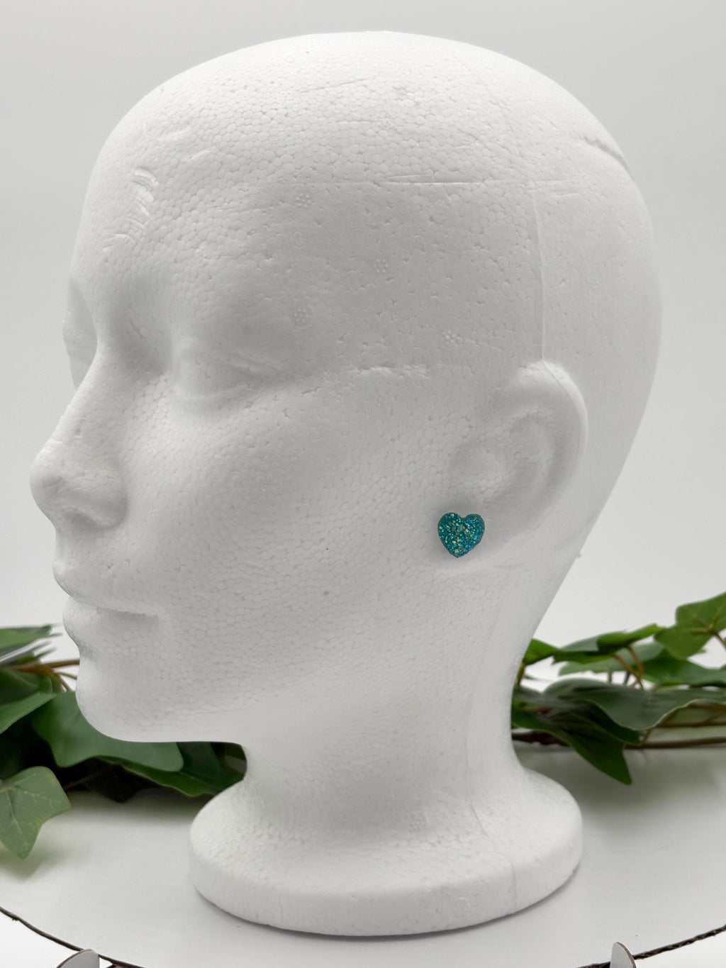 Mannequin head with a sparkling blue heart-shaped earring on a white background