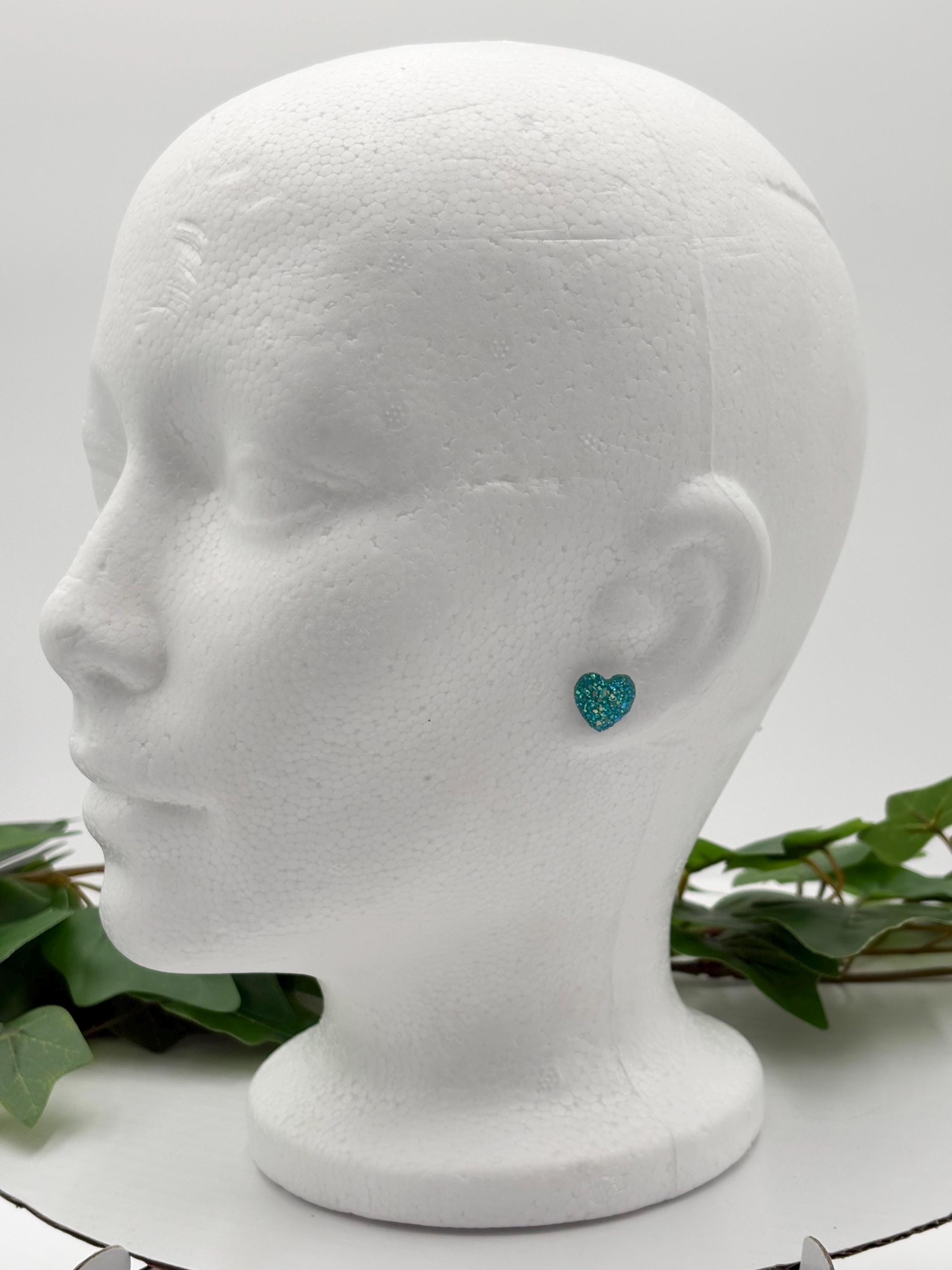 Mannequin head with a sparkling blue heart-shaped earring on a white background