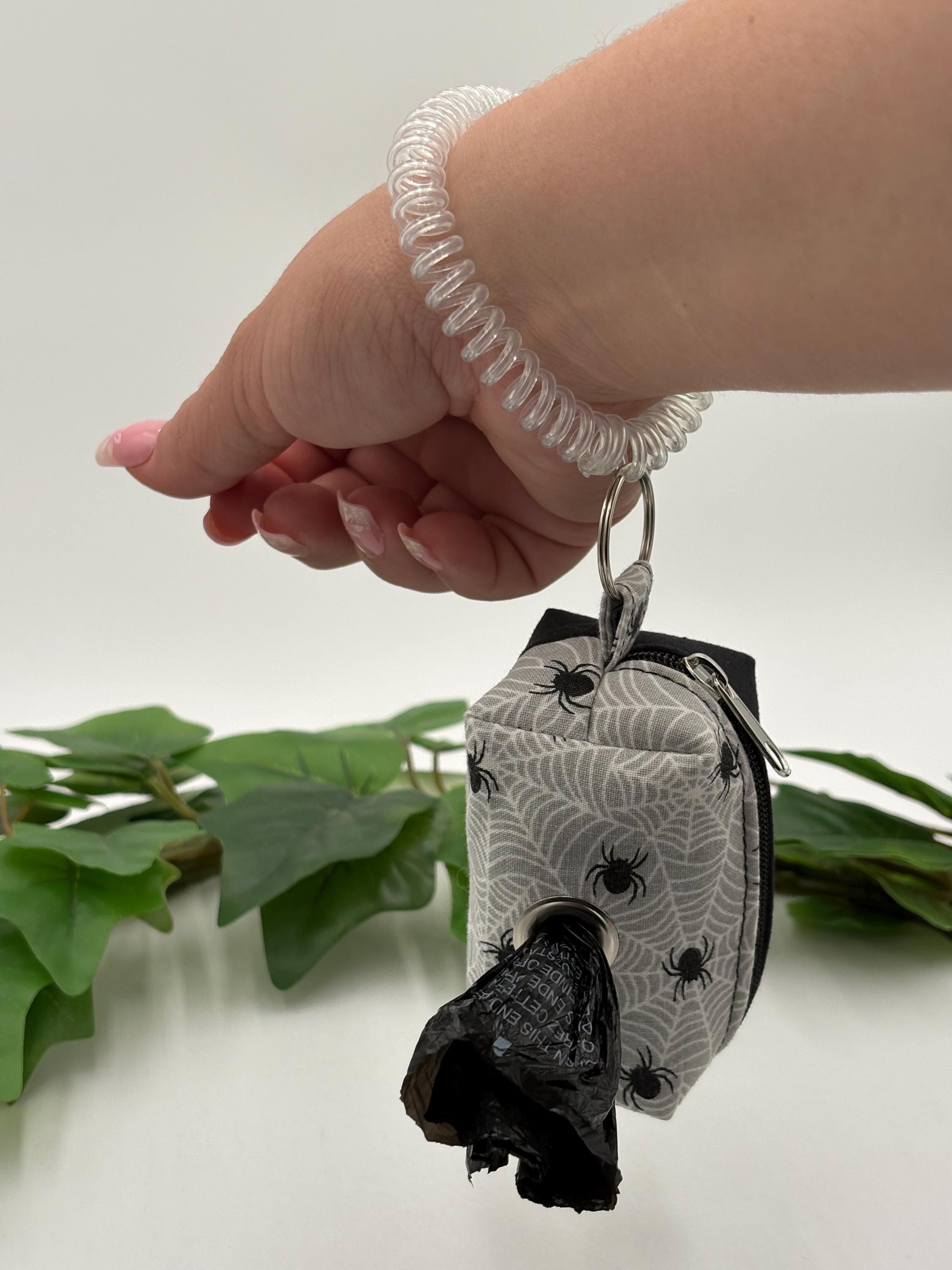 Hand holding a dog poop bag holder with spiral coil with a spider web pattern on a white background