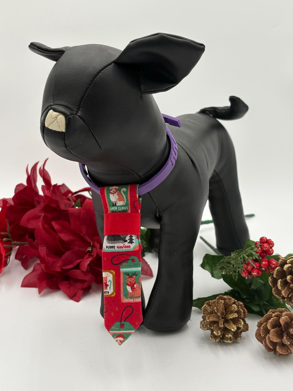 Black dog mannequin standing with a Red Christmas-themed over the collar necktie with festive designs on a white background with poinsettias and a pine cone.