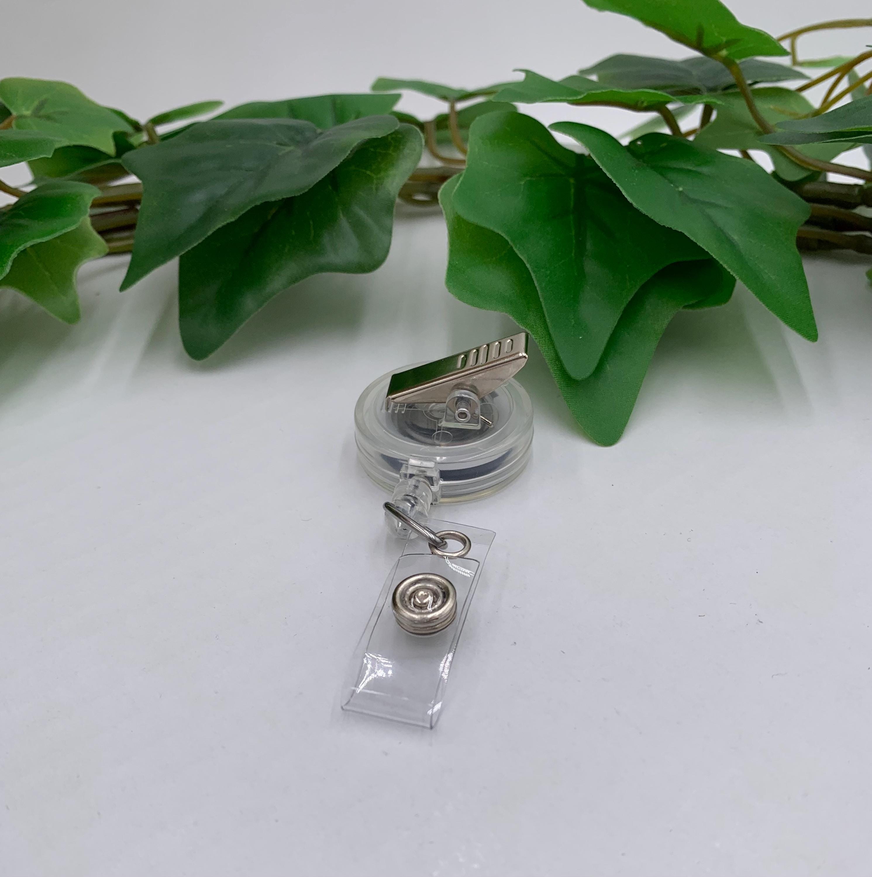 Clear badge holder with a clip on a white surface with green leaves in the background