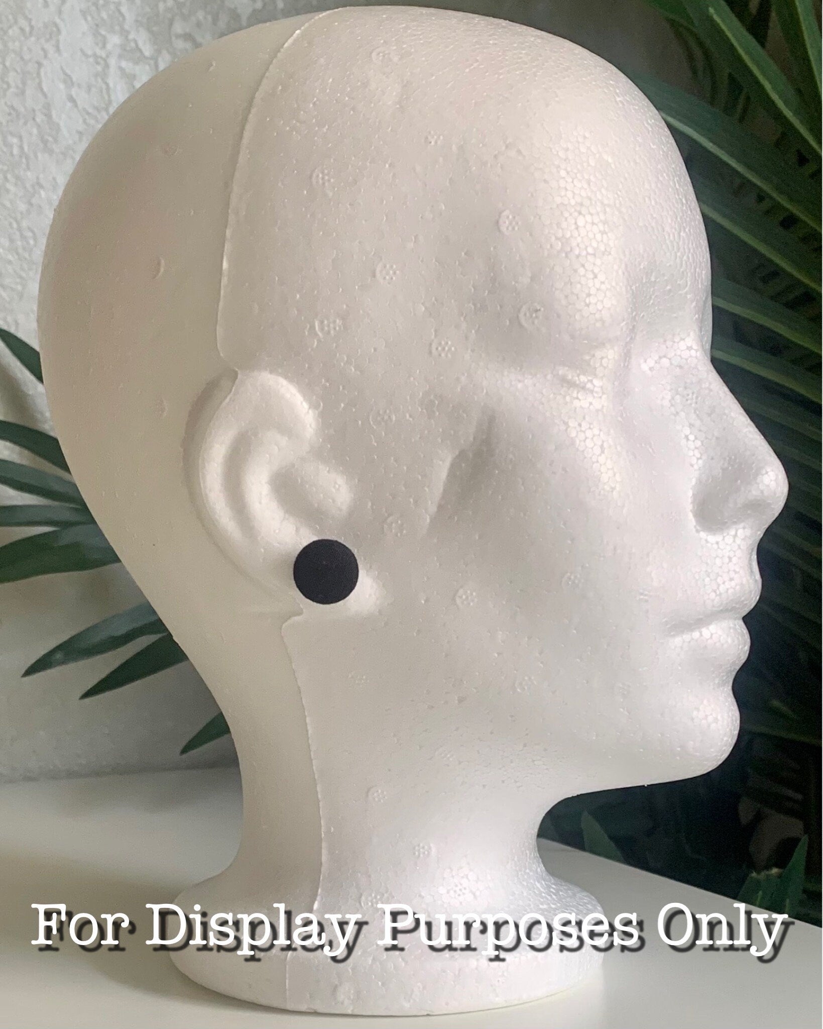 Mannequin head with a black dot on an ear against a neutral background that says "For Display Purposes Only"