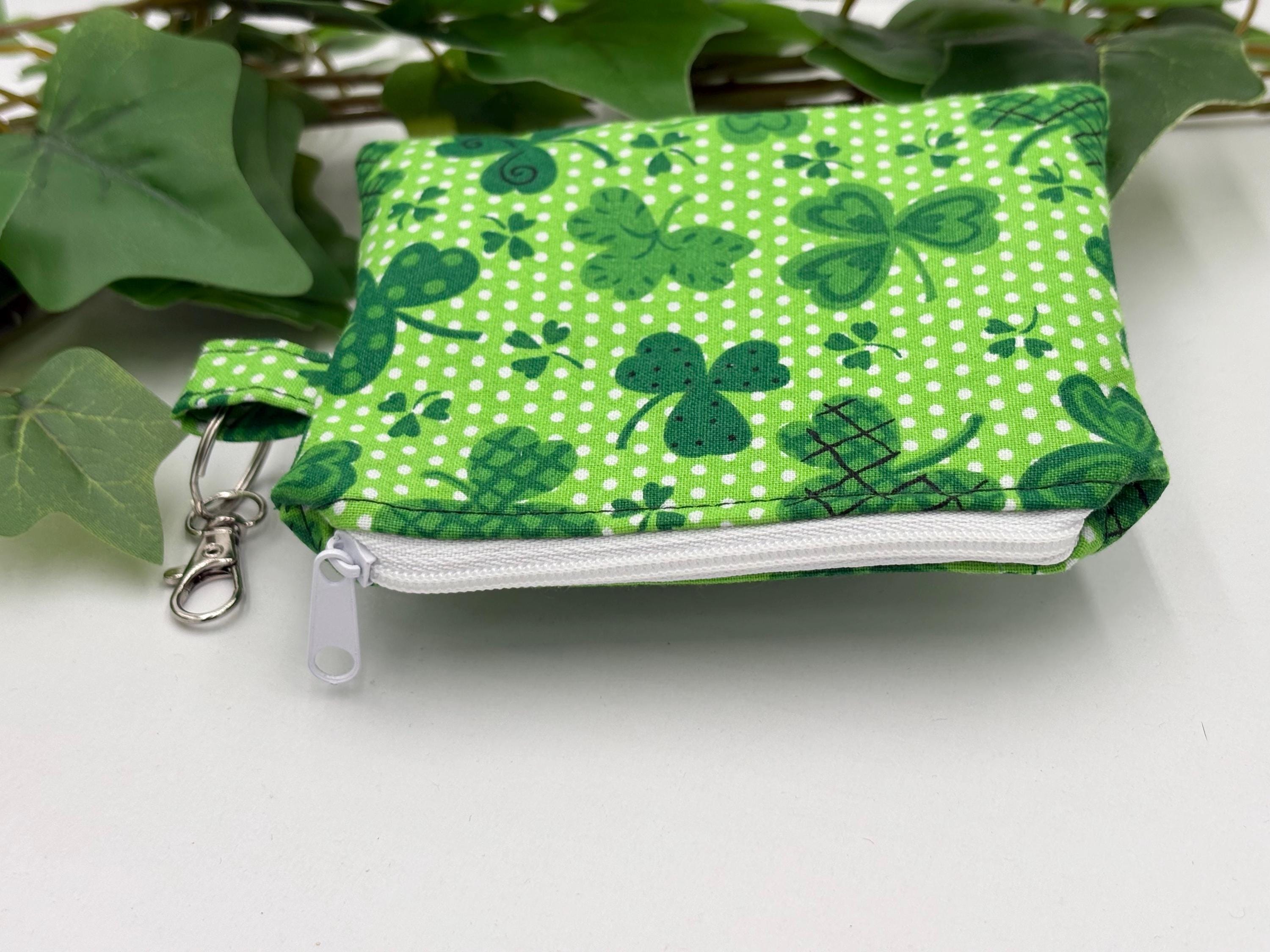 Small coin purse keychain with green shamrocks pattern with white zipper on a white background with green leaves