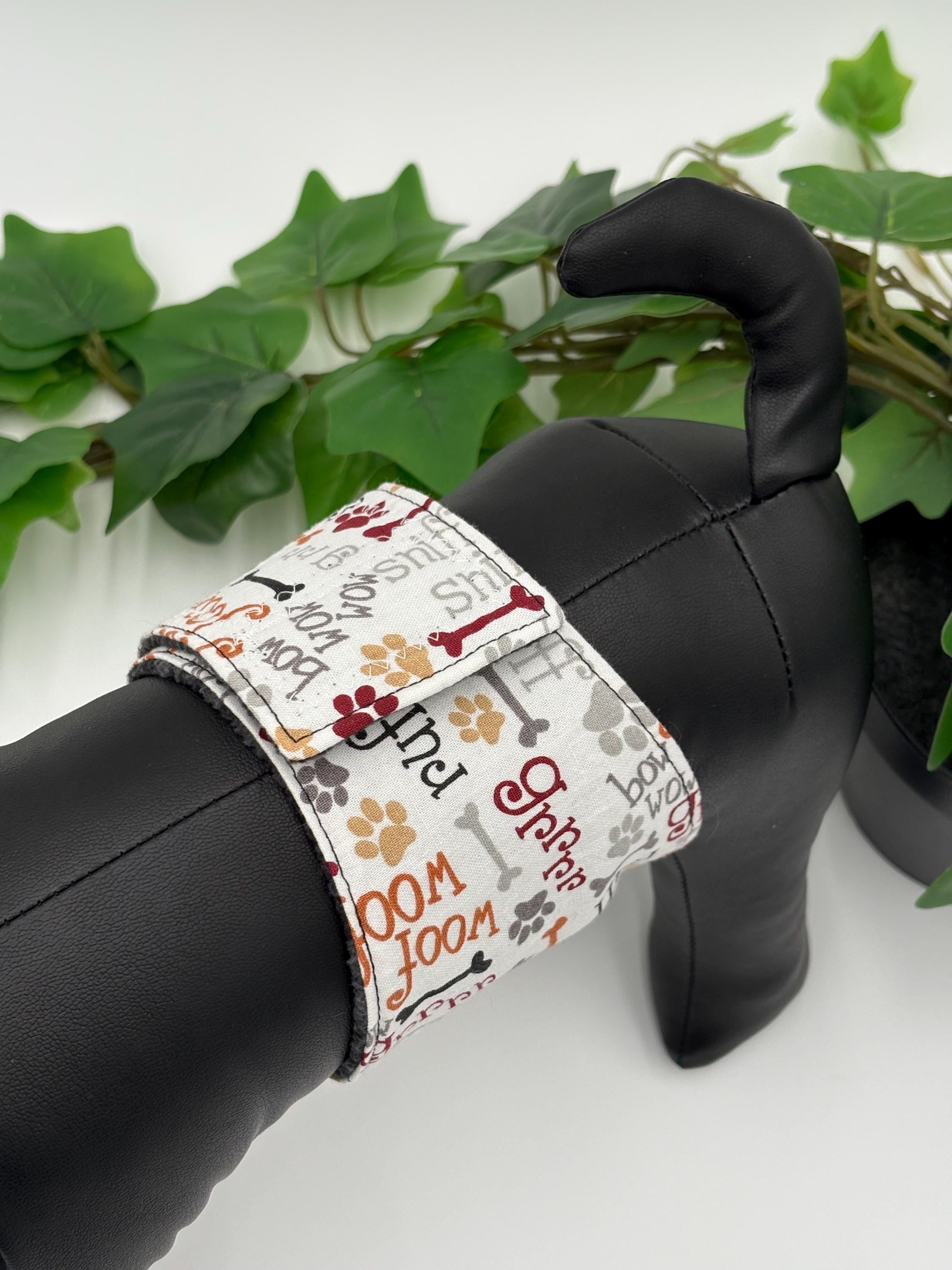 close up birdseye view of Black dog mannequin with a patterned belly band on a white background standing next to potted plant