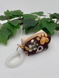 Small fabric dog poop bag holder with paw print design on a white surface with green leaves in the background