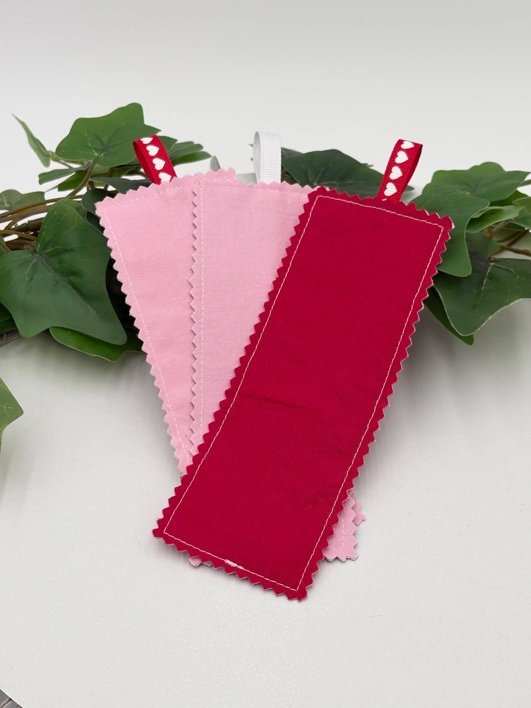 Two red and one pink fabric bookmarks on a white background with green leaves.